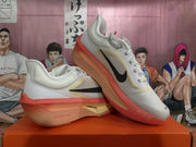 Pair of white Nike running shoes with black Swooshes, pale yellow trim, and coral soles, shown at an angle.