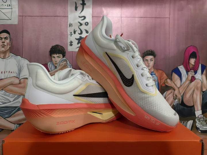 Pair of white Nike running shoes with black Swooshes, pale yellow trim, and coral soles, shown at an angle.