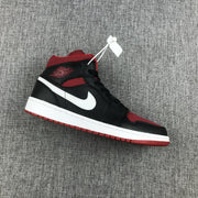 Side view of a black, red, and white Jordan Air Jordan 1 Mid sneaker on gray fabric.