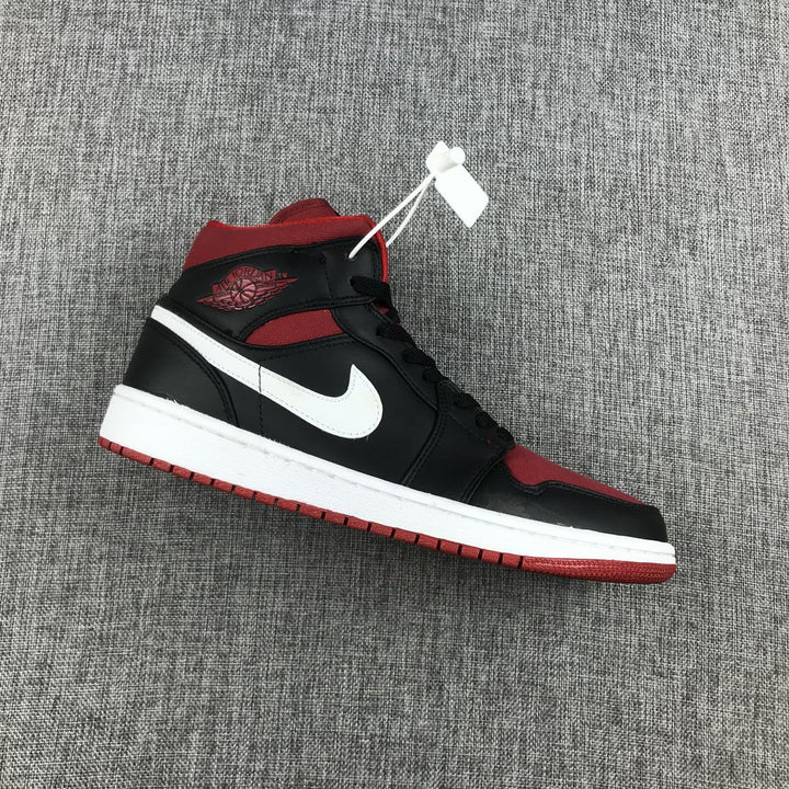 Side view of a black, red, and white Jordan Air Jordan 1 Mid sneaker on gray fabric.