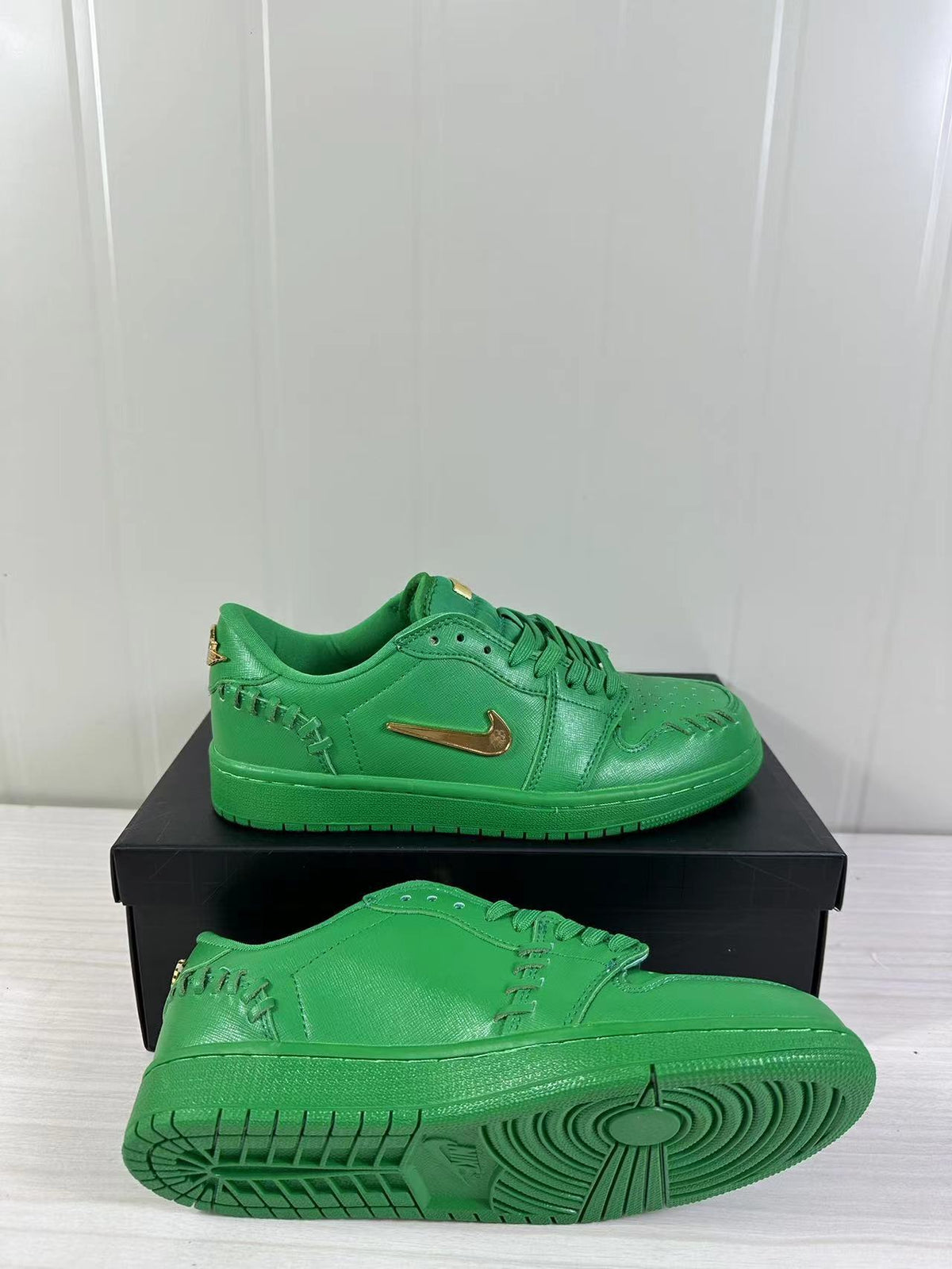 Green low-top sneakers with metallic gold Swoosh details shown on a black shoe box, including an outsole view.