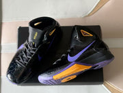 Pair of black Nike high-top basketball shoes showing purple and gold accents and patterned soles