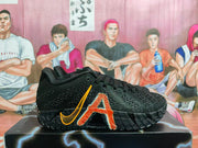 Side view of a black basketball shoe with orange graphics, a small visible “ZOOMX” marking, and a textured outsole.