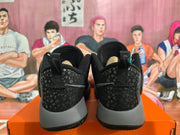Rear view of black and grey Nike basketball sneakers showing patterned heel panels, pull tabs and textured outsoles on an orange shoebox.