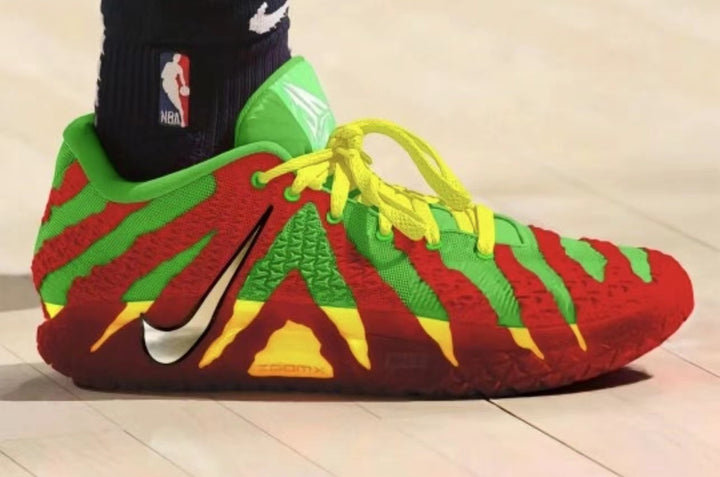 Side view of red, green, yellow and dark burgundy Nike basketball sneakers with yellow laces and a visible Swoosh, beside an NBA-branded sock.