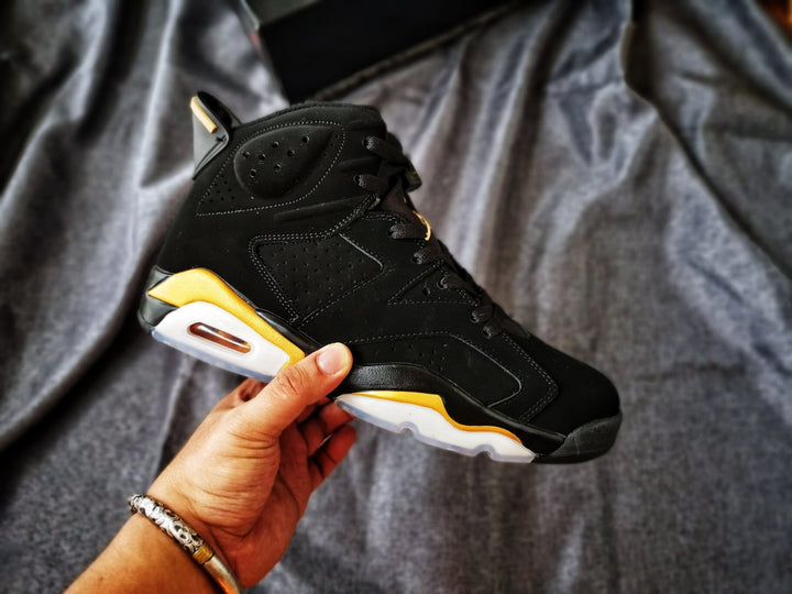 Side view of a black and gold Jordan Air Jordan 6 high-top sneaker held against a gray fabric background.