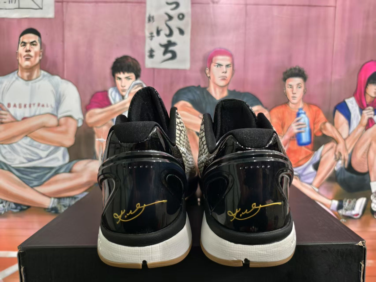 Rear view of black and beige Nike basketball sneakers showing glossy black heel panels, gold signature-style detailing, white midsoles, and gum-colored outsoles.