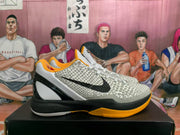 Side view of one basketball sneaker showing the textured upper, black Nike swoosh, black midsole, and gold-orange outsole.