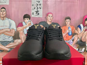Front view of black basketball sneakers showing the lace-up design, perforated toe boxes and gold tongue details.