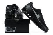 Black and silver Nike Air Max 90 sneakers beside a shoebox; the box label shows a sample size.