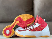 Low-angle product view with one shoe showing the red and gold traction outsole.