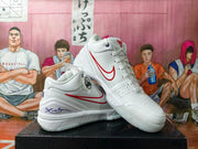 Angled view of white basketball shoes with red side detailing and Kobe-themed graphics