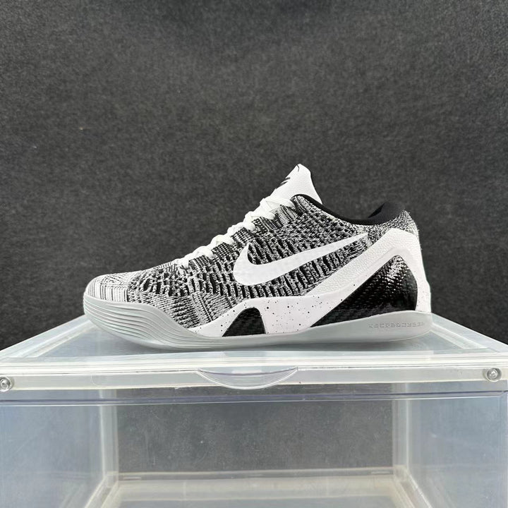 Gray and black Nike low-top sneaker with a textured upper, white Swoosh, white laces, and contrasting midsole displayed on a clear stand.