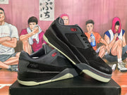 Angled view of two black and grey low-top sneakers, highlighting the side panels, red accents, textured toe areas, and light-colored outsole.