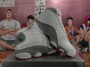 Angled view of two white and gray high-top Jordan sneakers showing the perforated uppers, gray lower panels, red outsole accents, and tongue branding.