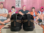 Rear view of black Nike Book 1 sneakers showing Chapter One heel markings, tan-gold trim, and black soles on a box.