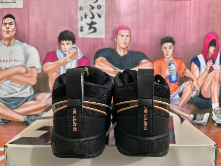 Rear view of black Nike Book 1 sneakers showing Chapter One heel markings, tan-gold trim, and black soles on a box.