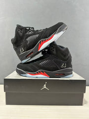 Two black Air Jordan 5 sneakers arranged on a shoe box, showing the red-and-translucent outsole sections.