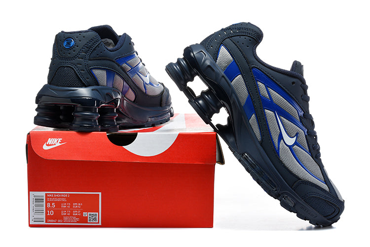 Nike Shox Ride 2 sneakers in navy, silver-gray, and blue displayed with a shoebox; the box label shows a sample size.