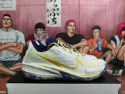 Side profile of a white Nike basketball sneaker with a gold swoosh, yellow trim, purple outsole, and speckled midsole.