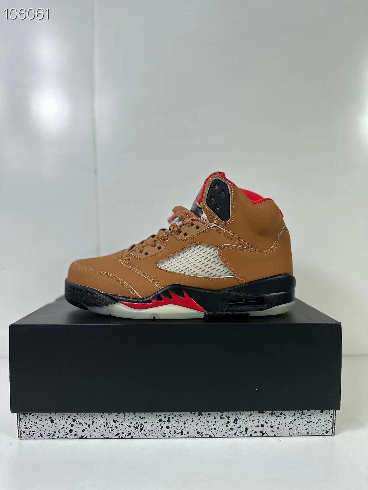 Brown high-top sneaker shown in profile on a black shoebox, with red accents and a black midsole.