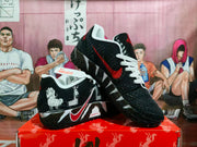 Black, white and red sneakers displayed on an orange box, showing textured panels, white laces, red accents, and character artwork.