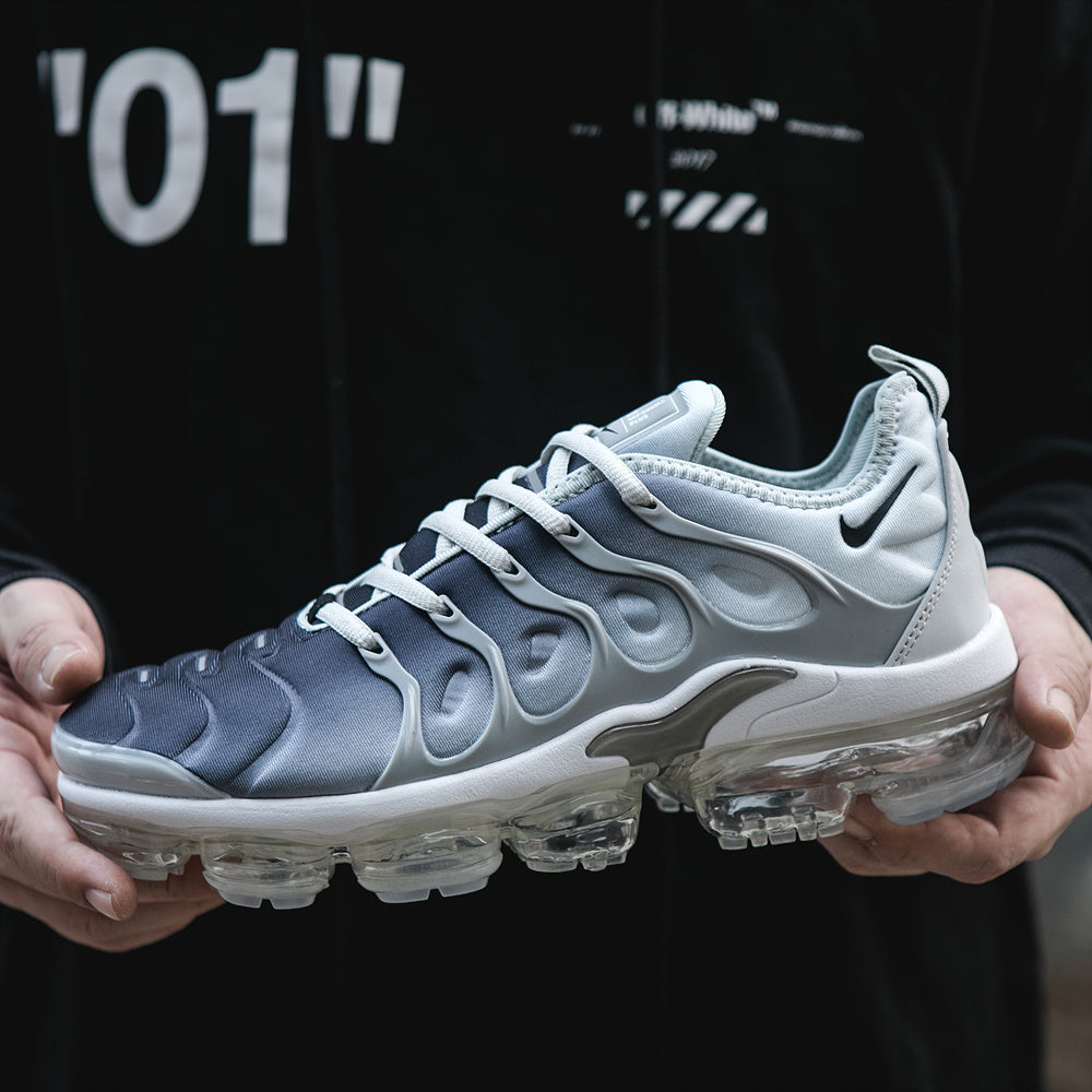 Close-up side view of grey, black, and white Nike Air VaporMax Plus sneakers