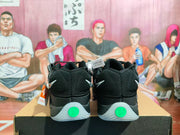 Rear view of black Nike basketball sneakers showing mesh heel panels, white Swoosh details, translucent outsoles, and green heel accents.