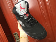 Single black high-top sneaker held at an angle, showing the lacing area, silver side panel, and white tongue.