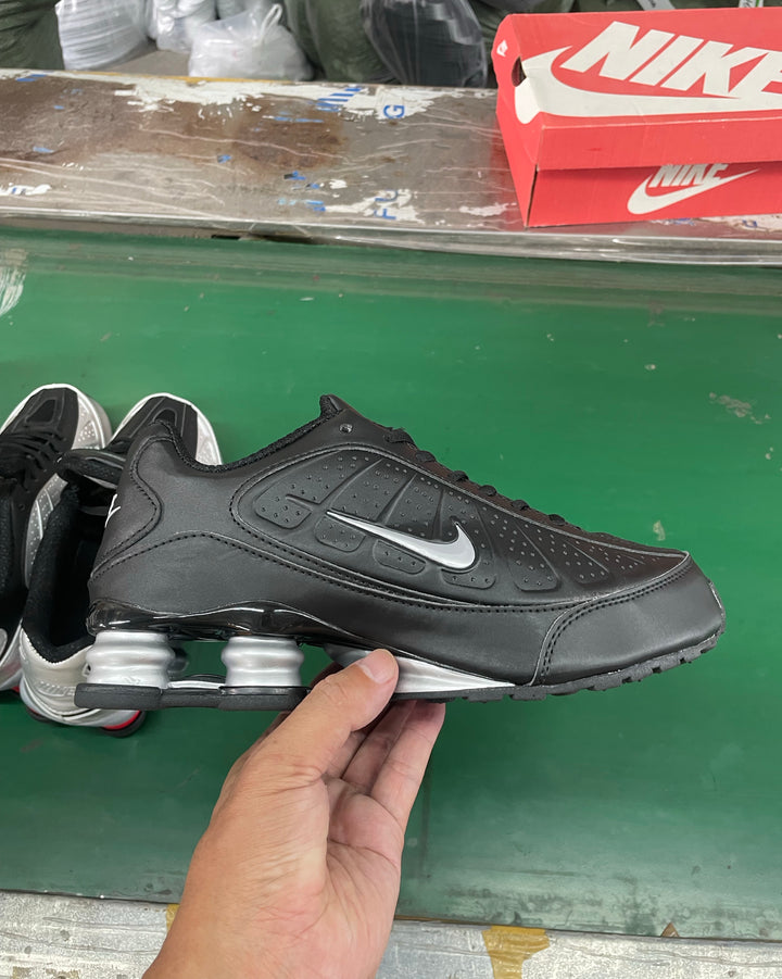 Side view of a black and silver Nike sneaker with perforated panels and visible heel cushioning, held in front of a Nike shoebox.