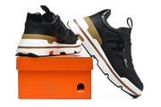 Black sneakers displayed beside an orange shoe box, showing the side panels and chunky soles.