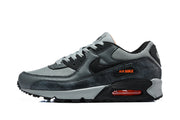 Side profile of a grey and black Nike Air Max 90 sneaker with orange accents and a visible Air unit.