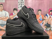 Angled view of two black Nike sneakers displayed on a shoebox, highlighting the side Swoosh and lace-up construction.