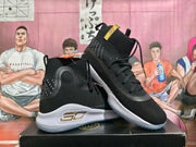 Angled view of black high-top shoes with gold-tone side accents and white soles.