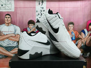 Angled side view of white Nike basketball sneakers with large black Swoosh logos and contrasting outsole sections.