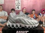Side profile of a silver Nike sneaker showing the Swoosh, layered upper panels, and circular sole elements.