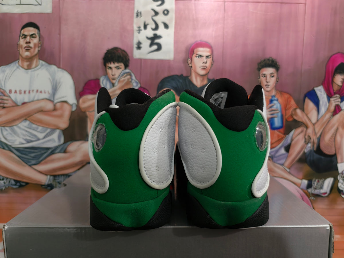 Rear view of white and green high-top basketball sneakers with black collars and outsole accents, displayed on a box.