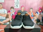 Front view of the black sneakers with orange tongue logos, black laces, and white midsoles.
