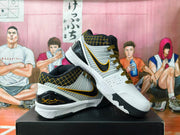 Pair of white, black, and gold Nike basketball shoes shown from the side and at an angle.