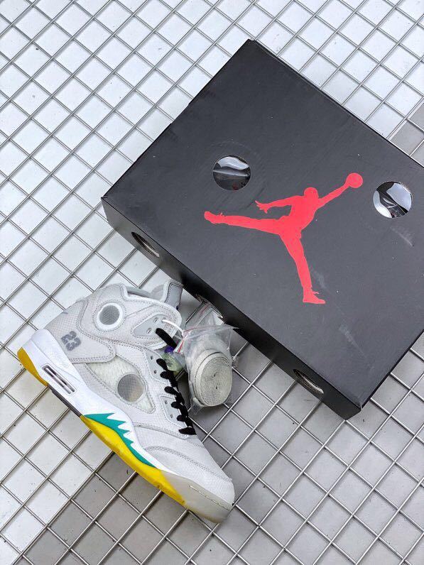 Grey and white high-top sneaker beside a black Jordan shoebox, showing yellow and teal outsole accents.