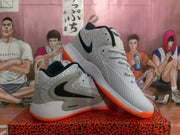 Angled view of white Nike basketball sneakers with black side branding, speckled gray panels, gray laces, and orange outsoles.