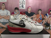 Side view of a white basketball sneaker with black Swoosh branding, red midsole, perforated panels, and a circular side emblem.