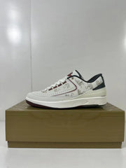 Side profile of a white low-top sneaker showing dragon-pattern panels, perforations, dark red trim, and a dark outsole.