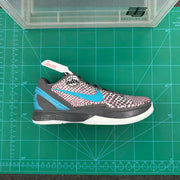 Single sneaker shown on a green cutting mat, highlighting the patterned upper, blue Swoosh, dark trim and white sole.