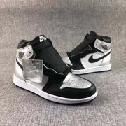 Front three-quarter product view showing the perforated silver toe box, black overlays, white midsole, and second shoe in the background.