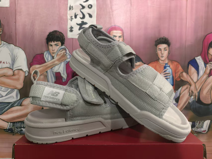 Pair of grey New Balance adjustable strap sandals displayed from an angled side view.
