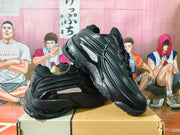 Angled side view showing the sculpted panels and sole of the black sneakers.