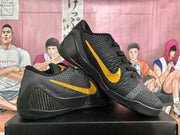 Angled view of the black and gold basketball sneakers showing the gold Swoosh, textured side panels, and black soles.