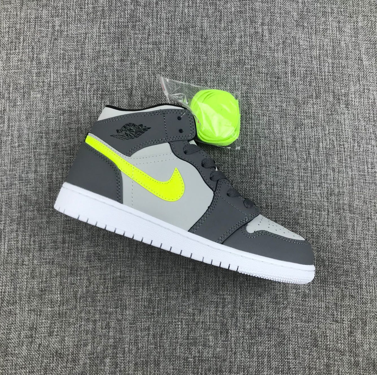 Side view of a grey and charcoal Jordan mid-top sneaker with fluorescent volt branding, white outsole and an extra fluorescent lace set.