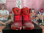 Front view of paired red high-top basketball sneakers showing red laces, textured toe boxes, Kobe Bryant logos on the tongues, and contrasting white outsole accents.